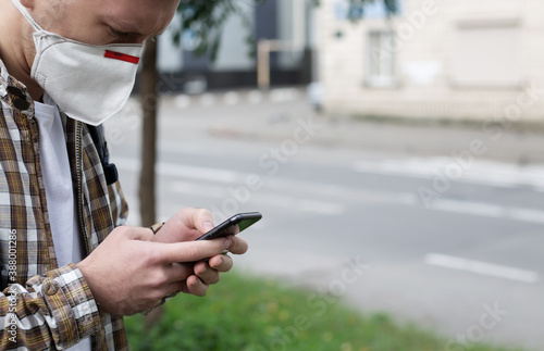 Young guy in a protective mask uses a smartphone on the street