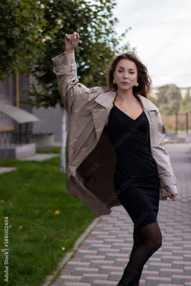 attractive slim young brunette in fashionable trench coat and black dress.