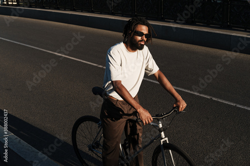 Serious african american guy riding bicycle at city bridge