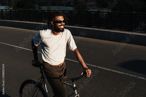 Happy african american guy smiling while riding bicycle at city bridge