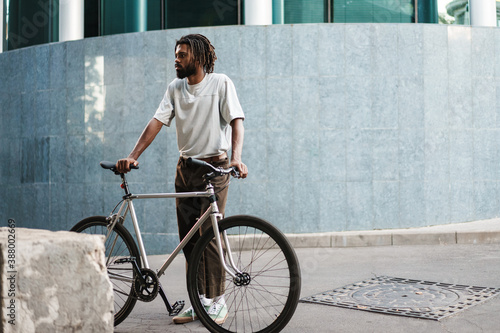 Handsome african american guy posing with bicycle at city street