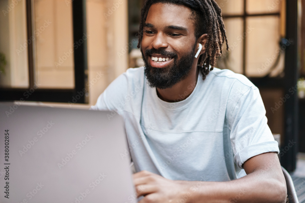 Fototapeta premium Cheerful african american guy in earphones working with laptop