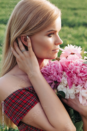 Beautiful young woman with long curly hair posing near peonies in a garden. The concept of perfume advertising. photo