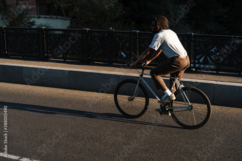 Fototapeta Naklejka Na Ścianę i Meble -  Happy african american guy smiling while riding bicycle at city bridge