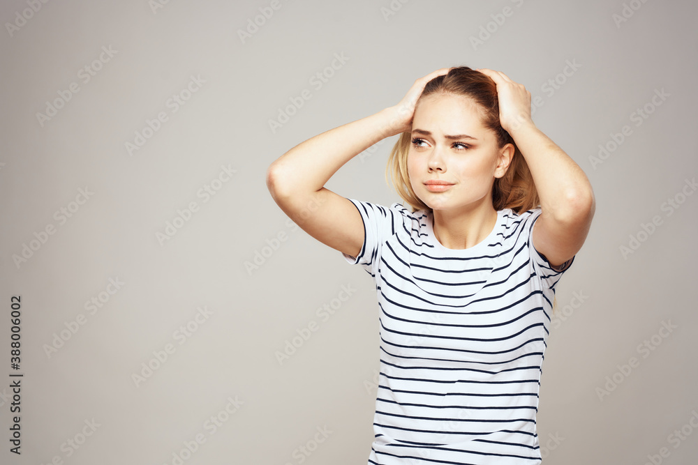 A woman in a striped T-shirt holds her hands in front of her emotions displeasure light background A woman in a striped T-shirt holds her hands in front of her emotions displeasure light background