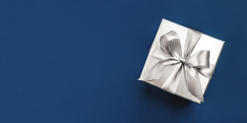 Silver gift box with bow on blue background. Flat lay, top view. Banner with copy space for text.