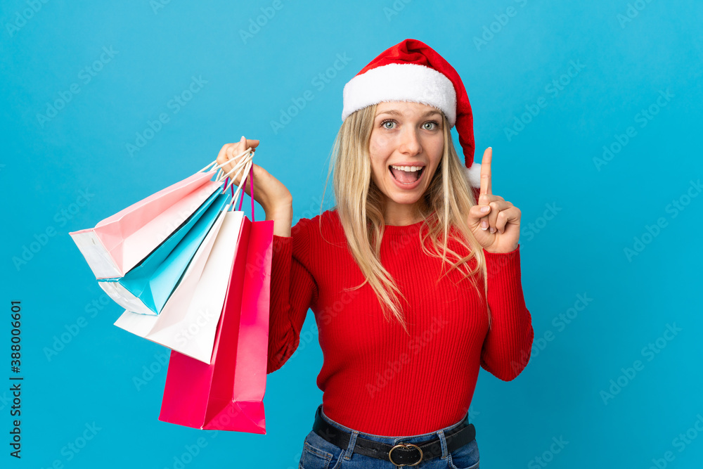 Obraz premium Woman with christmas hat going to buy something isolated on blue background pointing up a great idea