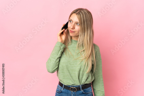 Young blonde woman isolated on pink background keeping a conversation with the mobile phone with someone © luismolinero