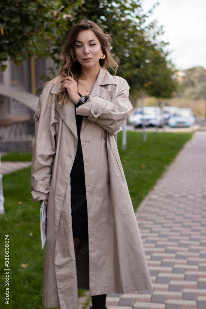 attractive slim young brunette in fashionable trench coat and black dress with a newspaper.