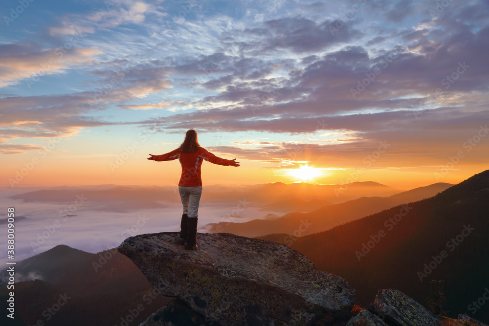 Landscape with beautiful sunrise, cloudy sky and orange colorful horizon. Mountains in the foggy morning. Successful sporty girl is standing at the edge of the precipice. Autumn.