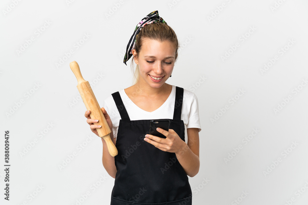 Young woman holding a rolling pin isolated on white background sending a message with the mobile Young woman holding a rolling pin isolated on white background sending a message with the mobile