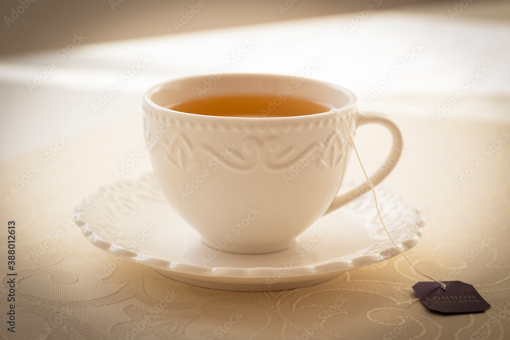 White festive cup with black tea and tea bag built on a beige tablecloth. White festive cup with black tea and tea bag built on a beige tablecloth.