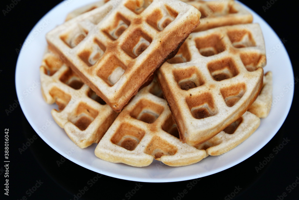 Belgian waffles in white plate on black glass table. Healthy breakfast, pieces of freshly baked classic wafer Belgian waffles in white plate on black glass table. Healthy breakfast, pieces of freshly baked classic wafer