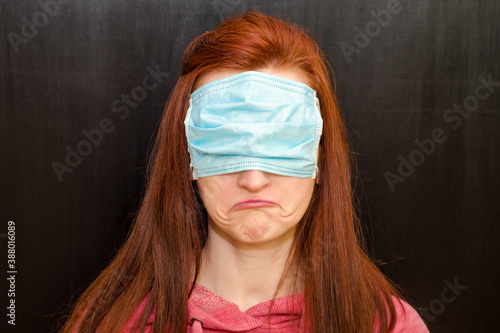 Photos Young caucasian redhaired girl with green eyes, in wrong used medical mask, on b