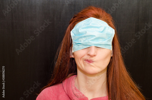 Young caucasian redhaired girl with green eyes, in wrong used medical mask, on black background, coronavirus epidemic