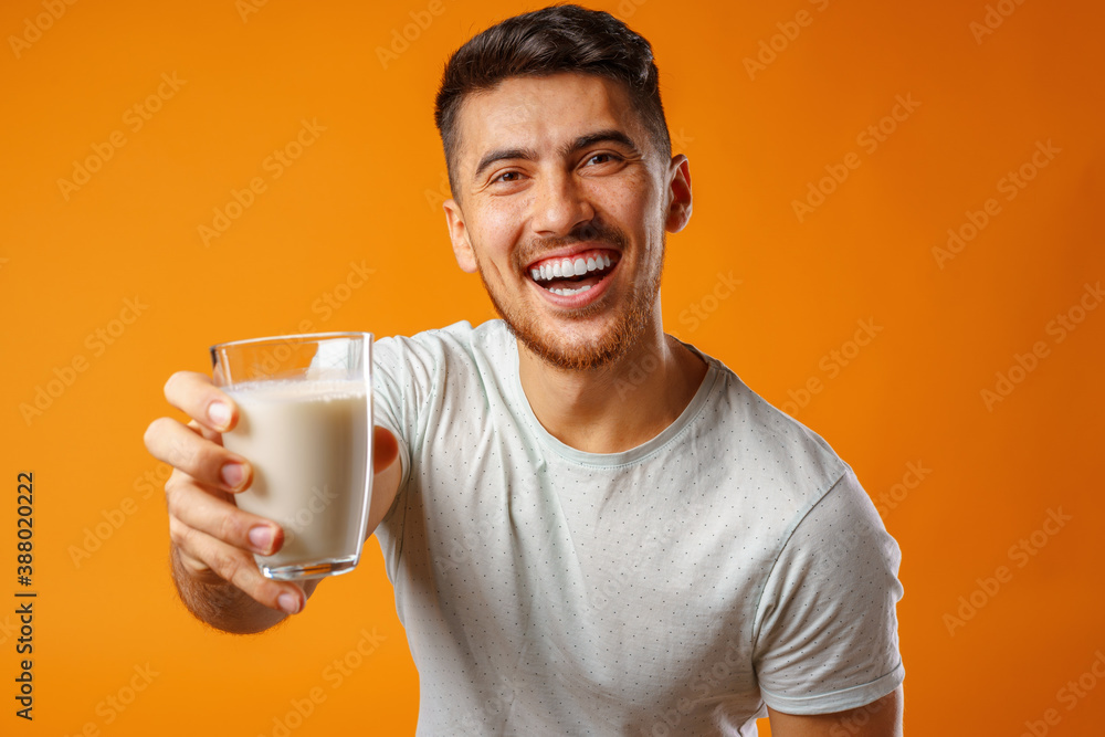 Happy smiling mixed-race man holding milk against yellow background Happy smiling mixed-race man holding milk against yellow background