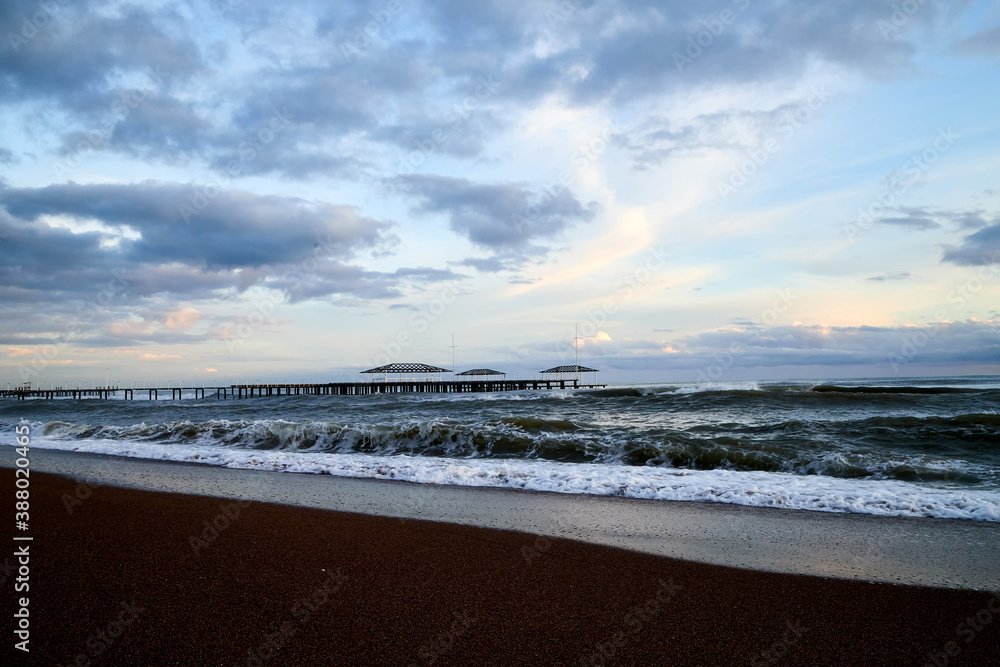 View from beach to water of sea, waves with white foam, pierce and sky with clouds in a nice evening. View from beach to water of sea, waves with white foam, pierce and sky with clouds in a nice evening.