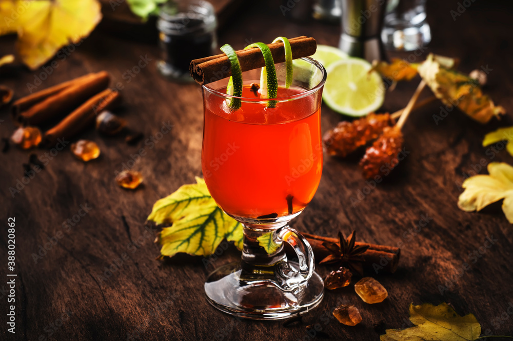 Hot rum punch, grog, autumn or winter warming alcoholic cocktail with dark rum, port, honey, lime juice, black tea, cinnamon and cloves in tall glass on vintage wooden background - obrazy, fototapety, plakaty 