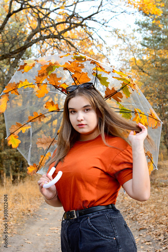 Vertical portrait of a girl under an umbrella with leaves in the autumn forest.