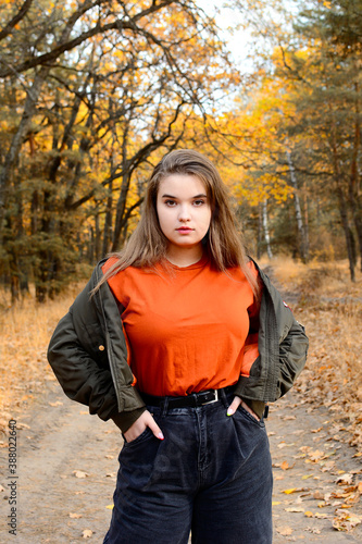 A young modern girl in fashionable clothes stands against the background of an autumn forest. Portrait.