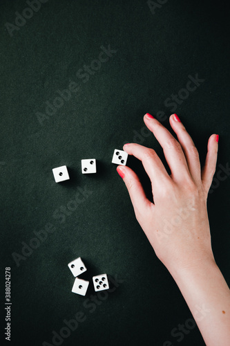 Female hand making a number sequence with rolling dices. White square dices against a dark green background.