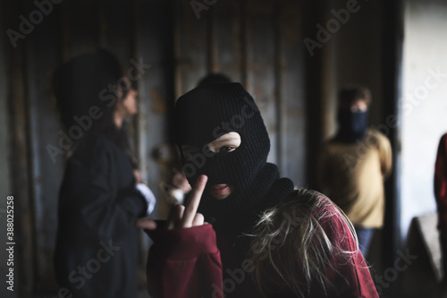 Girl with mask from teenagers gang standing indoors in abandoned building, showing middle finger. photo