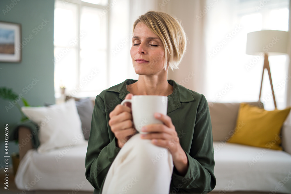 Portrait of woman meditating indoors in office, holding cup of tea.