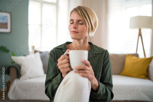 Portrait of woman meditating indoors in office, holding cup of tea.
