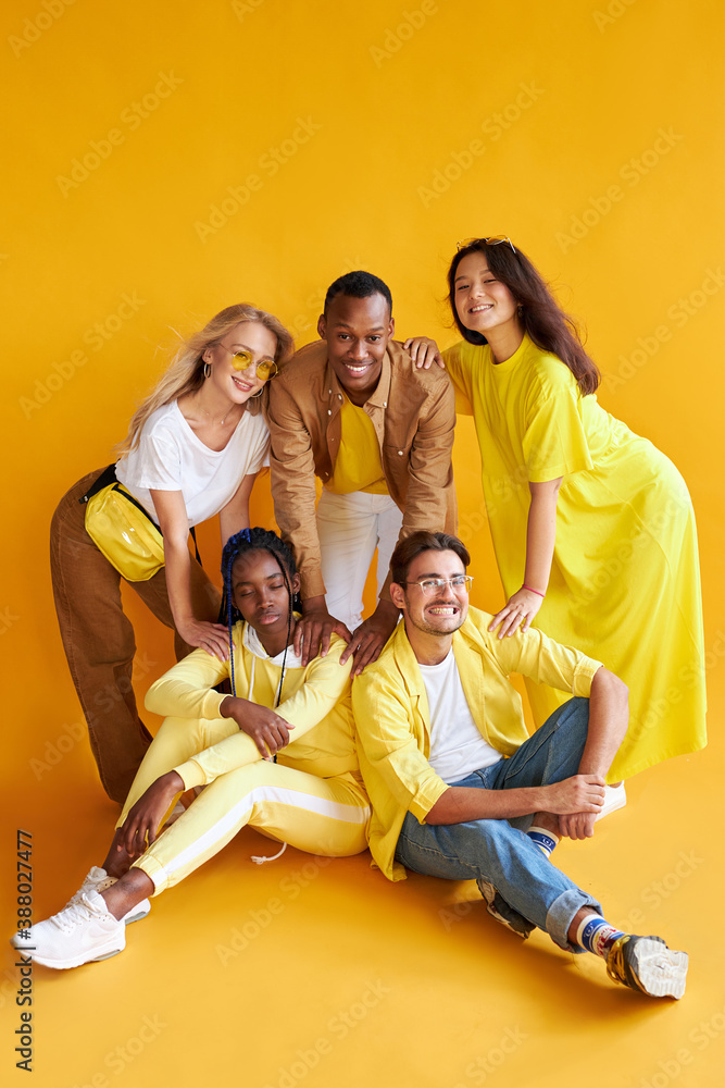 group of happy diverse young men and women isolated on yellow background, five friendly mixed race models, wear stylish yellow clothes posing at camera