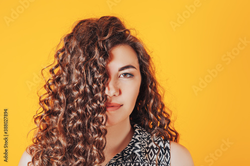 Beautiful woman with curly hair posing at camera on yellow background