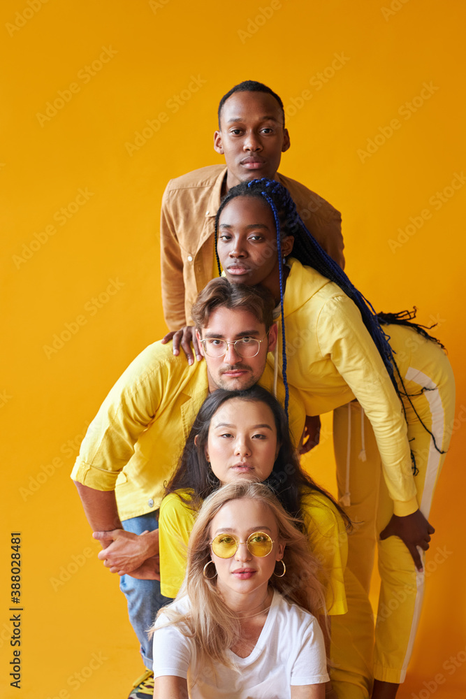 students from different countries in studio with yellow background, mixed race people in one group, friendly stylish people posing, look at camera