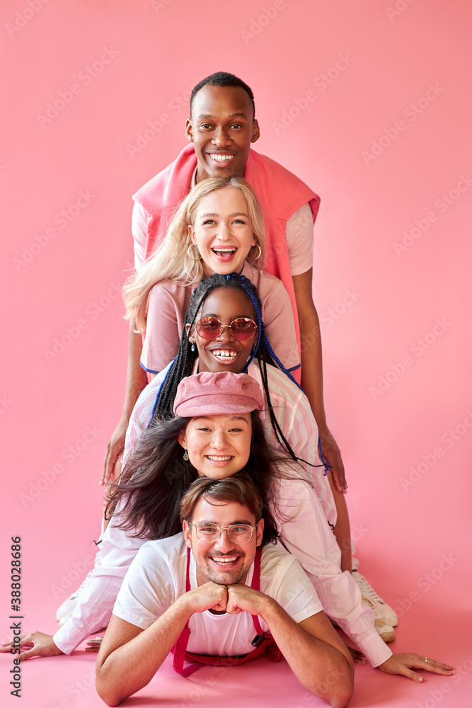 smiling mixed race group of people in studio on pink background, attractive ladies and handsome guys in cool stylish wear outfit