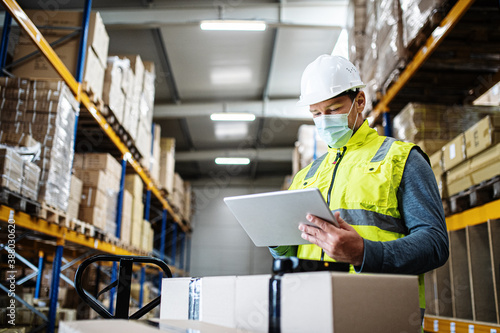 Man worker with tablet working indoors in warehouse, coronavirus concept.