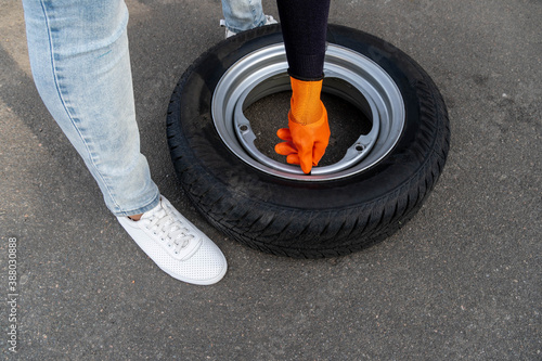 a woman in orange gloves unscrews the nipple cover on a car wheel.