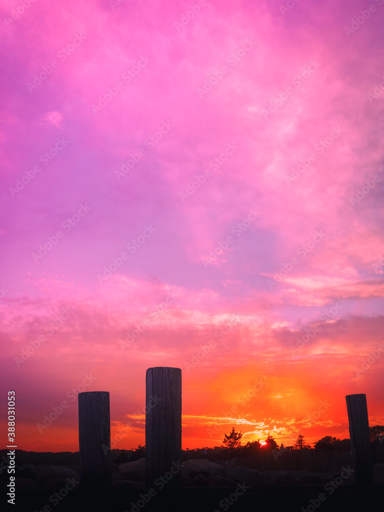 Pink sunset cloudscape over the horizon with trees in distance and three large poles in the blurred foreground Pink sunset cloudscape over the horizon with trees in distance and three large poles in the blurred foreground