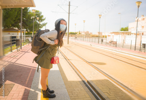 young happy and attractive Asian woman traveling during new normal - beautiful Chinese girl with backpack waiting for train at station platform as tourism in virus time
