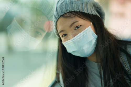 Фотография lifestyle portrait of young attractive and pretty Asian woman wearing mask in ra