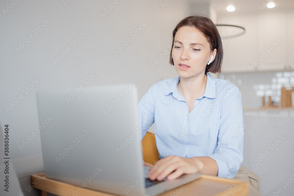 Young woman working remotely from home office on couch in kitchen behind laptop internet in headphones. Lifestyle communication work Young woman working remotely from home office on couch in kitchen behind laptop internet in headphones. Lifestyle communication work