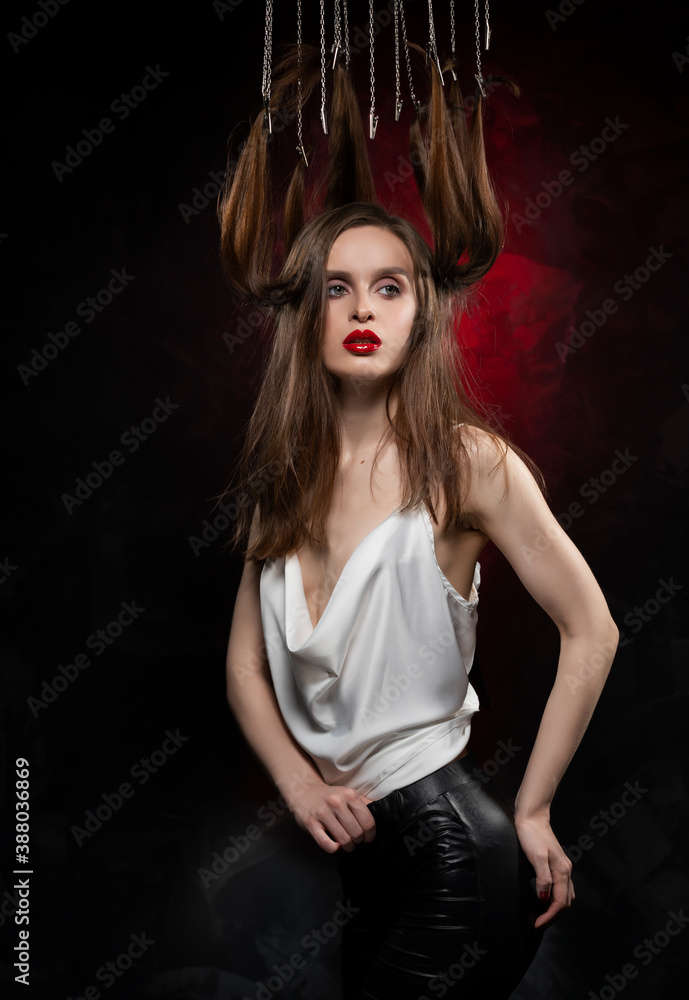 Φωτογραφία A beautiful girl with evening make-up and red lips wearing a blouse with a deep neckline and her hair suspended on chains, posing on a red and black background
