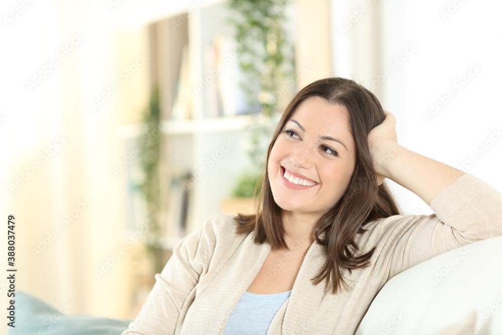 Happy woman thinking looking at side sitting at home