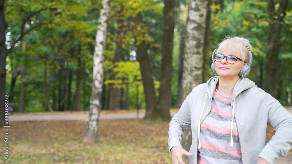 Senior Active Woman Walks in the Park or Forest and Listens to Music on Headphones. Portrait Mature Female Relaxing in Nature. Rest and Calm Retired Woman Enjoys Life Outdoors. Leisure and Lifestyle Senior Active Woman Walks in the Park or Forest and Listens to Music on Headphones. Portrait Mature Female Relaxing in Nature. Rest and Calm Retired Woman Enjoys Life Outdoors. Leisure and Lifestyle