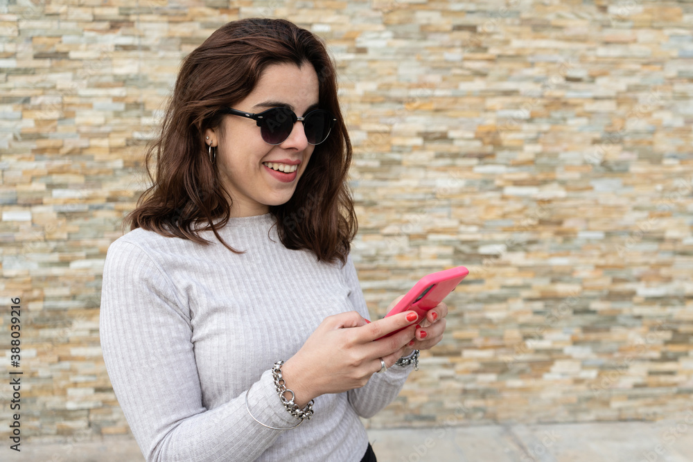 Diagonal view of young woman smiling while sending messages from her smartphone. Diagonal view of young woman smiling while sending messages from her smartphone.