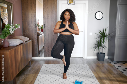 fat overweight black woman keep balance, stand on one leg, yoga time at home. concentrated on yoga, meditation. healthy lifestyle photo