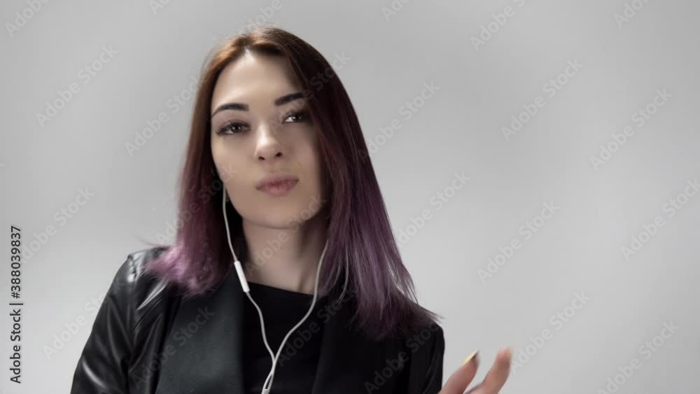 Portrait of a young cheerful woman with ear buds who is dancing on the white background. A pretty caucasian lady is listening to music holding a smartphone in her hand. She sings and looks satisfied. Portrait of a young cheerful woman with ear buds who is dancing on the white background. A pretty caucasian lady is listening to music holding a smartphone in her hand. She sings and looks satisfied.