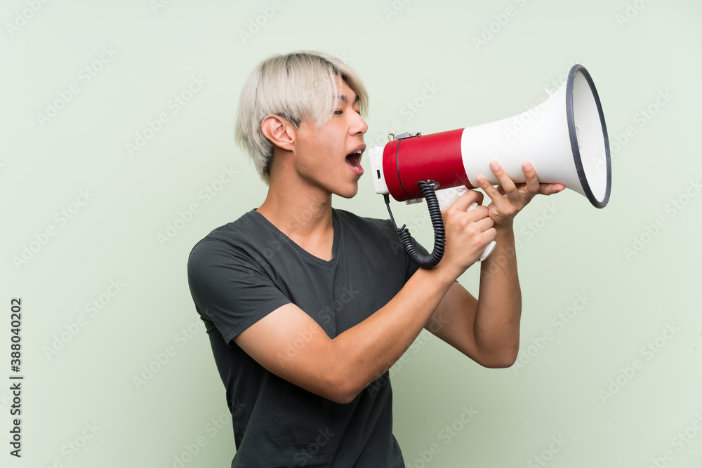 Young asian man over isolated green background shouting through a megaphone Young asian man over isolated green background shouting through a megaphone