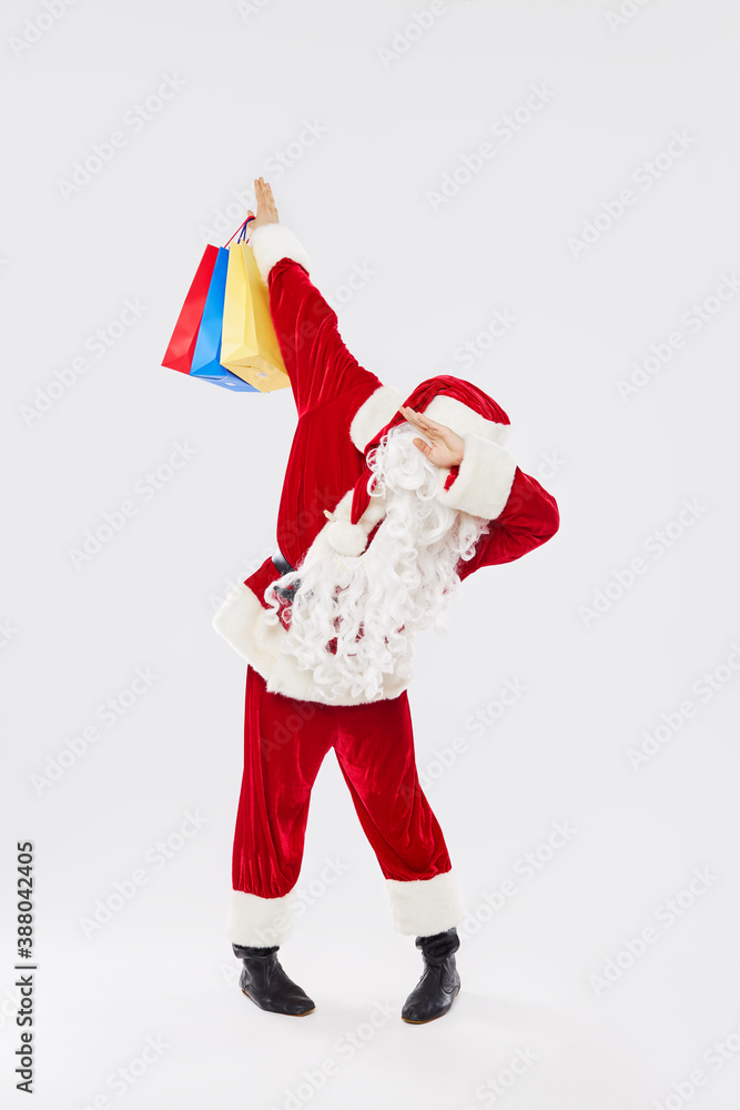 Joyful Santa claus on red costume dancing dab step with shopping bags and gifts on white background. Joyful Santa claus on red costume dancing dab step with shopping bags and gifts on white background.