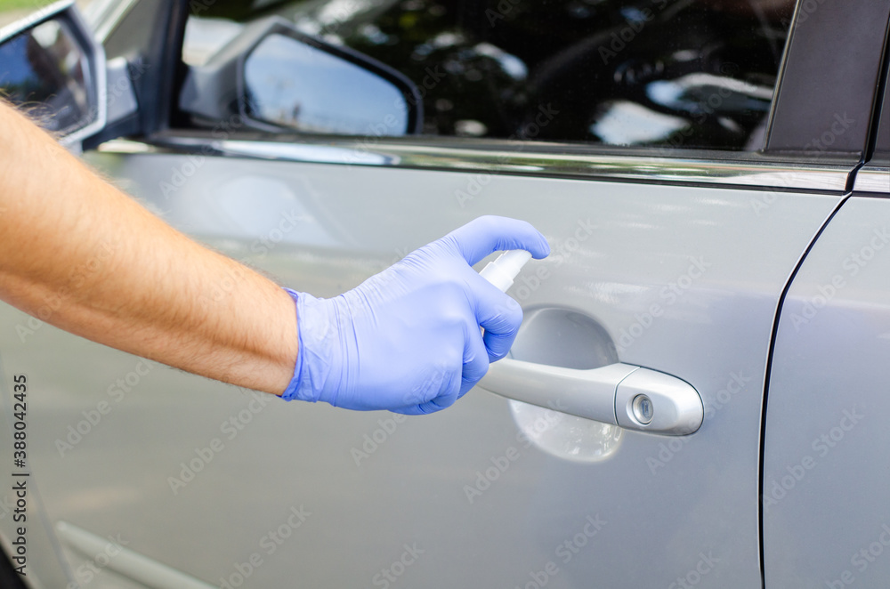 Man sanitizing door handle of his car outdoors. Male hand in protective glove holding sanitizer closeup. Man sanitizing door handle of his car outdoors. Male hand in protective glove holding sanitizer closeup.