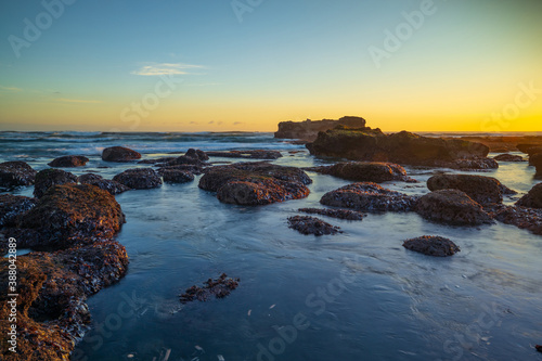 Beach during low tide. Amazing seascape. Stones covered by water. Sunset time. Golden hour. Slow shutter speed. Soft focus. Clear sky. Mengening beach, Bali, Indonesia