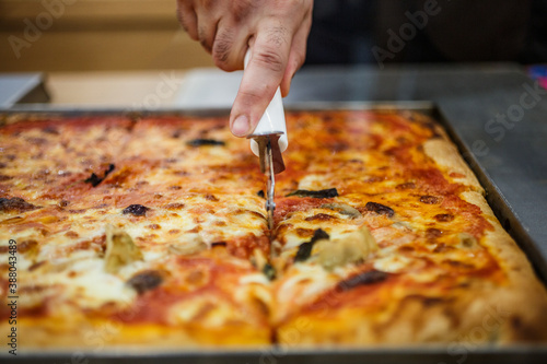 Pizza in teglia tagliata con una rotella tagliapizza direttamente nel banco di esposizione di una rosticceria photo