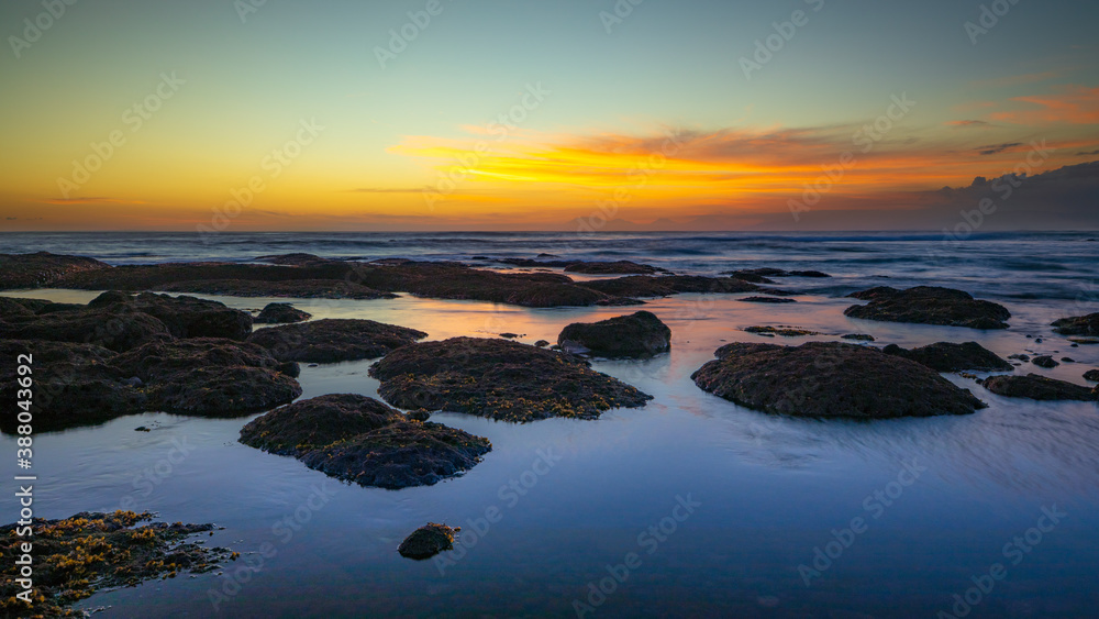 Beach during low tide. Amazing seascape. Stones covered by water. Sunset time. Golden hour. Slow shutter speed. Soft focus. Water reflection. Mengening beach, Bali, Indonesia